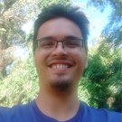 Retrato de de Herbherth, um homem jovem de pele clara. Ele está posicionado ao ar livre, olhando diretamente para a câmera com um sorriso aberto e radiante que transmite entusiasmo.