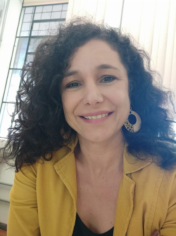 Retrato de Silvana, uma mulher branca de pele clara. Ela está centralizada na foto, olhando diretamente para a câmera com um sorriso suave e acolhedor.